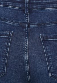 Granatowe dżinsy z denimu o dopasowanym kroju, średnim stanie i dwoma tylnymi kieszeniami z kontrastującym przeszyciem. Gładka faktura.