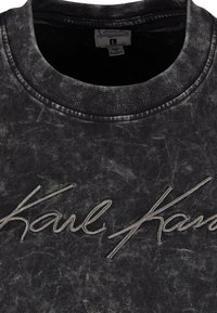 Sort sweatshirt med rund hals, der har en struktureret overflade og et broderet "Karl" logo i gråtværs over brystet.