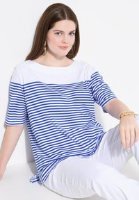 Modrý a bílý pruhovaný krátký rukáv top se širokým výstřihem a uvolněným střihem, doplněný bílými kalhotami a zlatým řetízkovým náramkem.