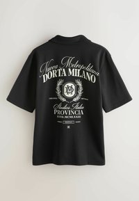Chemise noire à manches courtes avec texte blanc « Nuova Metropolitana Dorta Milano », emblème de couronne de laurier et inscriptions supplémentaires de style italien au dos.
