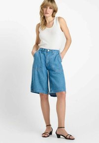 Denim bermuda shorts, middenblauw, hoge taille met frontzakken, opgerolde zoom, gecombineerd met een strak wit tanktop en zwarte sandalen.