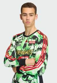 Lange mouw trui in zwart, groen en rood met een graffiti-achtig patroon. Voorzien van rode strepen op de schouders en een logo op de borst.