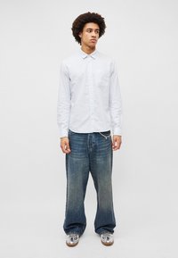 Ριγέ πουκάμισο με μακρύ μανίκι και κουμπιά σε ανοιχτό μπλε, με θήκη στο στήθος. Συνδυασμένο με φαρδιά, ξεθωριασμένα τζιν σε μπλε χρώμα και ασημένια παπούτσια.