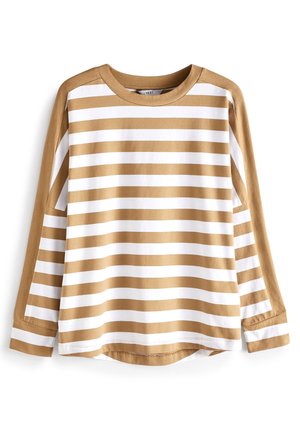 Femme portant un t-shirt à manches longues beige et blanc rayé, un pantalon cargo vert olive et des baskets blanches devant un mur bleu.