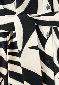 Tissu à motif abstrait noir et blanc avec ceinture nouée et boutons noirs sur un vêtement plissé.