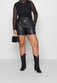 Czarne skórzane szorty z zakładkami i bocznymi kieszeniami, w połączeniu z czarną siateczkową bluzką z długim rękawem oraz czarnymi kowbojkami z dekoracyjnym haftem.