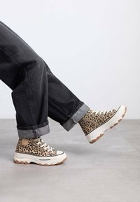 Zapatillas altas de estampado de leopardo con tela beige texturizada, suela de goma y entresuela blanca en contraste, combinadas con jeans negros de dobladillo.
