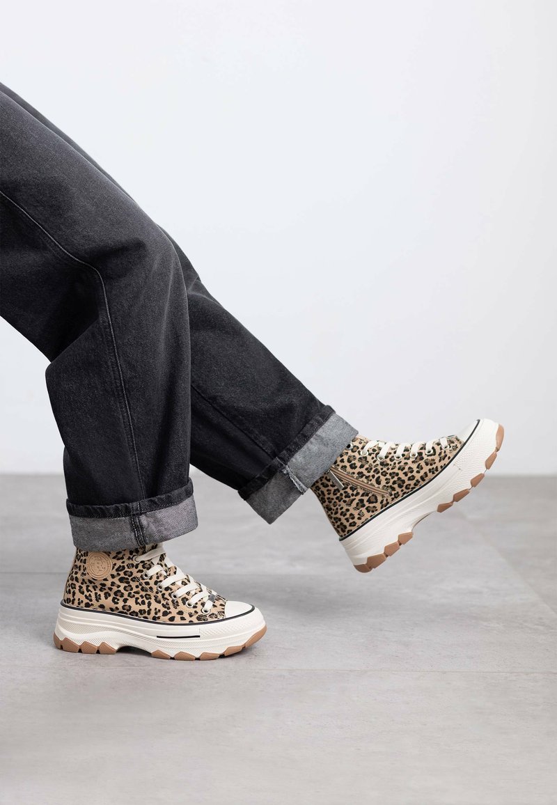 Zapatillas altas de estampado de leopardo con tela beige texturizada, suela de goma y entresuela blanca en contraste, combinadas con jeans negros de dobladillo.