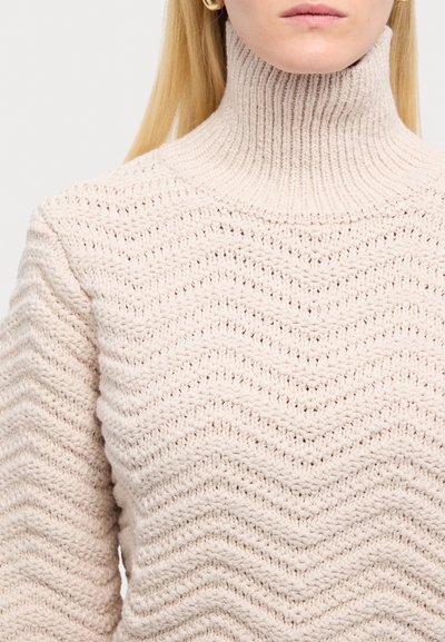 Pulover bej tricotat cu guler înalt, prezentând un model texturat ondulat și un guler cu nervuri. Designul include un material gros și moale.