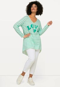 Tyrkis- och vitrandig långärmad tunika med "LOVE"-tryck, kombinerad med vit slim fit-byxor och beige sneakers med dragkedjor.