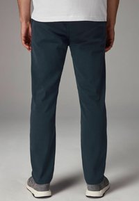 Pantalones azul oscuro de corte recto y textura suave, con un bolsillo trasero y combinados con zapatillas grises.