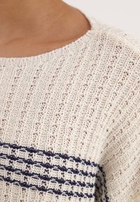 Maglione lavorato a maglia color crema con motivo a strisce verticali e linee orizzontali blu navy al centro. Collo a coste, strutturato.