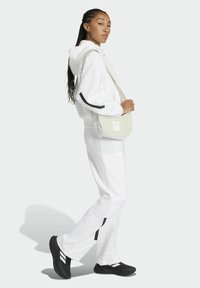 Sudadera con capucha blanca y pantalones jogger a juego con detalles negros; combinados con un bolso cruzado de color claro y zapatos negros con rayas blancas.