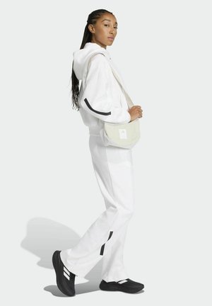 Felpa con cappuccio bianca e pantaloni della tuta abbinati con dettagli neri; abbinati a una borsa a tracolla di colore chiaro e scarpe nere con strisce bianche.