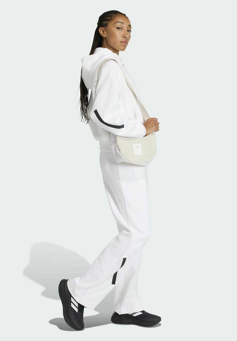 Sudadera con capucha blanca y pantalones jogger a juego con detalles negros; combinados con un bolso cruzado de color claro y zapatos negros con rayas blancas.