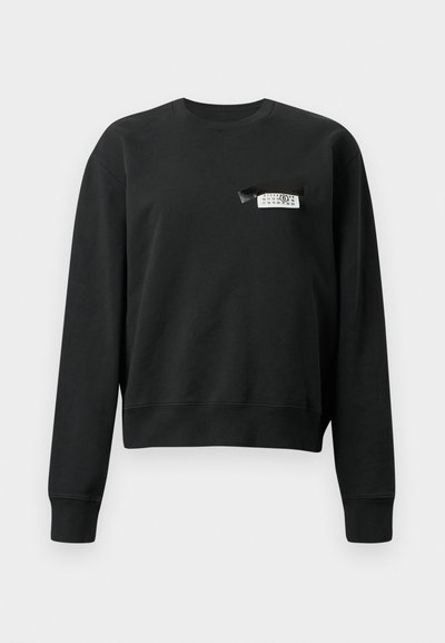 Črna dolga majica s crewneck izrezom in dolgimi rokavi z majhno belo in črno oznako, prišito blizu levega dela prsnega koša.