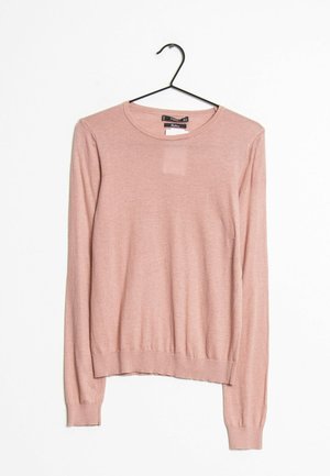 Pull rose clair à manches longues et col rond suspendu sur un cintre noir sur un fond blanc uni.