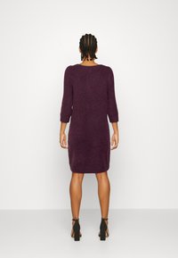 Abito a maglia viola fino al ginocchio, con maniche a tre quarti e scollatura rotonda, abbinato a sandali neri con tacco alto. Tessuto morbido, design semplice.