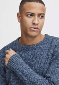 Pulover tricotat în nuanțe variate de albastru, având un model texturat și manșete cu diferite modele. Guler rotund și croială standard.