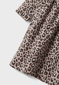 Tissu imprimé léopard en beige avec des taches marron foncé. Conception à manches courtes avec une texture douce et des détails de couture visibles.