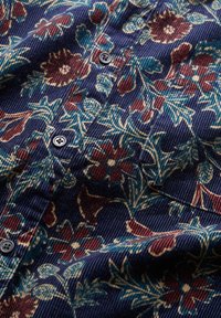Ziedu rakstains audums tumši zilos toņos, ar sarkaniem un ziliem ziediem. Ar teksturētu virsmu, kurā ir vertikālas korduroja līnijas un melni pogas.
