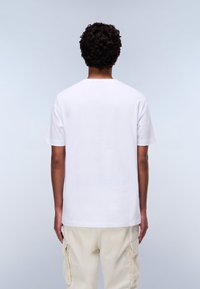 Hvid bomulds t-shirt med rund hals, vist fra ryggen. Casual pasform med korte ærmer, parret med cremefarvede cargo bukser.