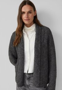 Gebreide donkergrijze cardigan met ribbeltextuur, open voorkant en wijde mouwen. Draag het over een witte blouse met kraag en stijl het met grijze broek.
