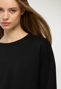 Felpa nera con scollatura rotonda, maniche lunghe e vestibilità comoda. Tessuto liscio con dettagli di cucitura visibili lungo il collo.