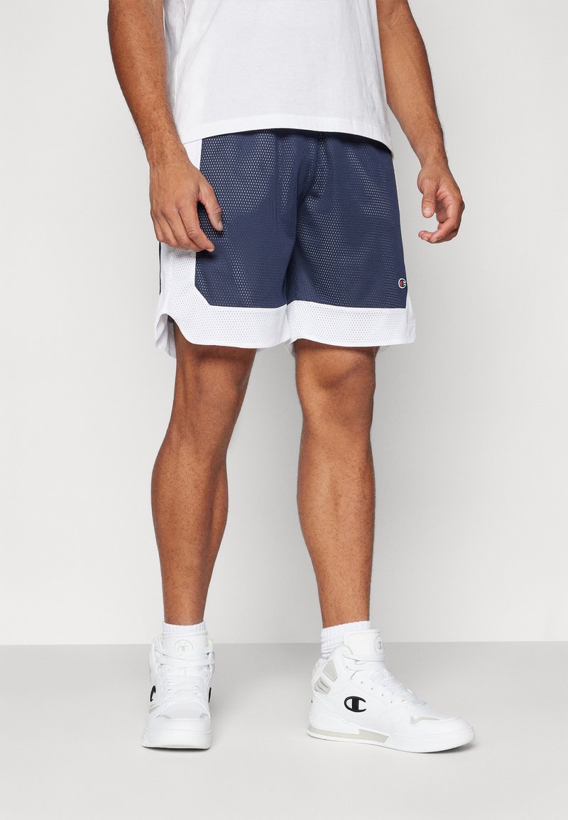 Mesh basketball shorts i navy blue og hvid, med et åndbart design og en kontrasterende hvid kant, parret med hvide højtop sneakers.