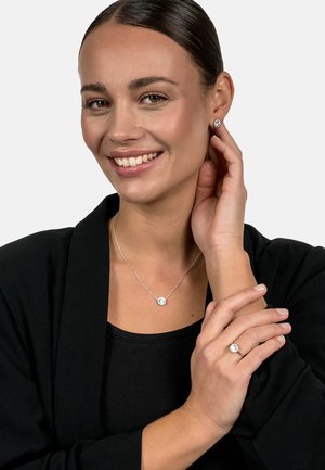 Silver necklace with a round pendant, matching stud earrings, and a ring featuring a central gemstone, all set against a black background.