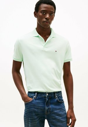 Polo de manga corta verde claro con cuello, que presenta un pequeño logo en el pecho. Combinado con jeans de mezclilla azul oscuro.