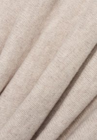 Hellbeige gestrickter Stoff mit einer weichen, strukturierten Oberfläche. Das Material weist ein dezentes Rippenmuster auf, das Variationen in der Fadenstärke zeigt.