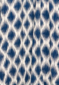 Biela látka s opakujúcim sa vzorom nepravidelných tmavomodrých diamantových tvarov a vertikálnych pruhov vytvárajúcich textúrovaný efekt.