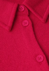 Helles pinkes Sweatshirt mit strukturiertem Strick, das einen Kragen und drei runde Knöpfe aufweist, die alle in der gleichen Farbe gehalten sind und ein einheitliches Erscheinungsbild schaffen.