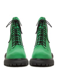 Groene suède enkellaarsjes met zwarte veters, voorzien van een ronde neus en een dikke, gestructureerde zwarte rubberen zool. Ritsdetails aan de zijkanten.