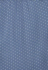 Tecido azul com pequenos bolinhas brancas. O tecido apresenta uma textura suave e forma pregas na parte de cima, criando um ajuste descontraído.