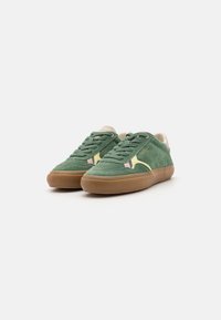 Zapatillas de ante verdes con un diseño en beige y rosa, puntera redondeada, suela de goma y acentos en contraste. Los cordones combinan con el material superior.