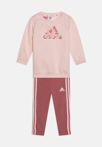 Felpa rosa chiaro con maniche lunghe e logo floreale di adidas; abbinata a leggings rosa scuro con strisce bianche laterali e logo.