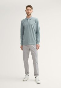 Lys blå langærmet polo shirt med krave, parret med lys grå opsmøgede bukser og hvide sko. Enkel design, ingen fremtrædende mønstre.