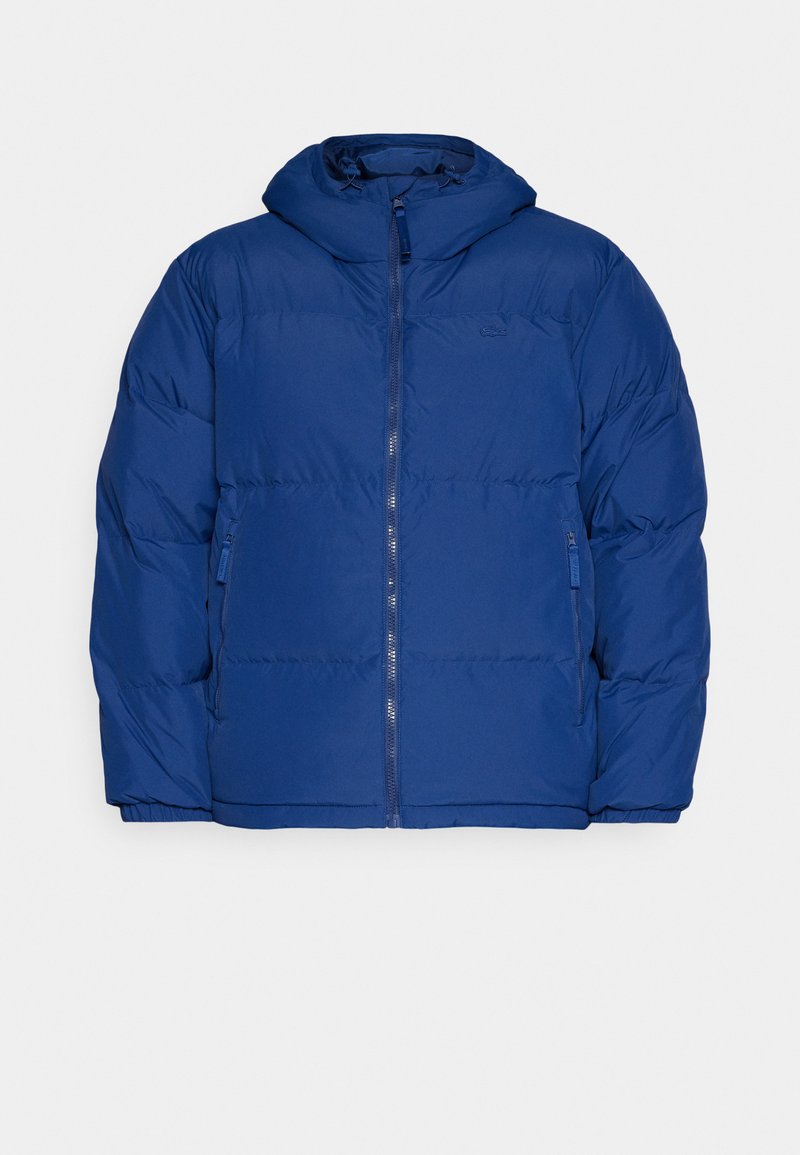 Giacca puffa blu con cappuccio, dotata di chiusura frontale con zip, polsini elasticizzati e due tasche laterali con zip. Tessuto liscio e imbottito.