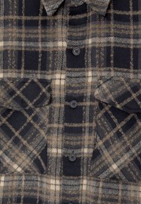Gros plan sur un tissu à carreaux foncé avec des boutons et deux poches poitrine sur une chemise ou une veste à col.
