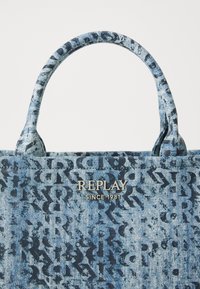 Denim-Tote-Bag mit einem blauen und schwarzen Buchstabenmuster und einer strukturierten Oberfläche. Akzentuiert mit einem metallischen "REPLAY SINCE 1981" Logo.