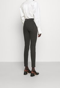 Pantalones ajustados en gris oscuro con un patrón sutil, que presentan una cintura alta y material elástico, combinados con zapatos de tacón negros.