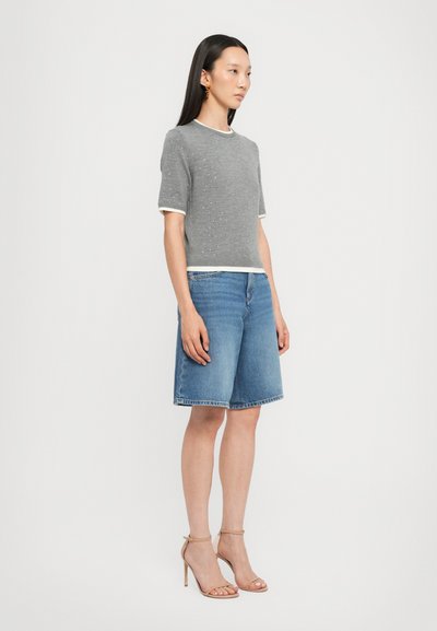 Gray knit sweater with white trim, paired with blue denim shorts. Model wears nude high-heeled sandals. Simple, modern aesthetic.