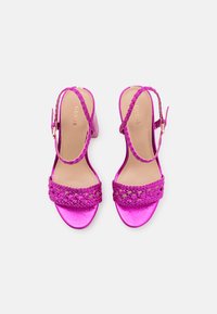 Sandalias de tacón fucsias con diseño de tira trenzada, punta abierta, hebilla ajustable en el tobillo y acabado metálico brillante.