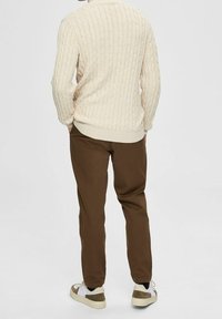 Kabelgebreid crèmekleurig sweater, bruine taps toelopende broek en witte sneakers met grijze accenten. Focus op textuur en eenvoudige ontwerpdetails.