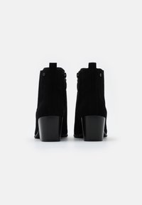 Czarne zamszowe botki za kostkę na słupku, wyposażone w boczne zamki błyskawiczne i tylne pętelki ułatwiające zakładanie. Gładka tekstura i minimalistyczny design.