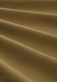 Tissu en coton marron avec une surface texturée, présentant un tomber fluide et des plis visibles, mettant en valeur des variations subtiles de teinte et de texture.