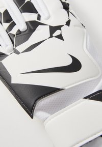 Nike-handskar med en vit bas som har ett svart geometriskt mönster, strukturerad design och en framträdande svart logotyp på utsidan.