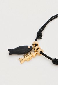 Μαύρο γοητευτικό φυλαχτό σε σχήμα ψαριού με υφή σχεδίου, με χρυσή σκελετωμένη διακόσμηση ψαριού, προσαρμοσμένο σε μαύρο πλεγμένο κορδόνι με χρυσό εξοπλισμό.